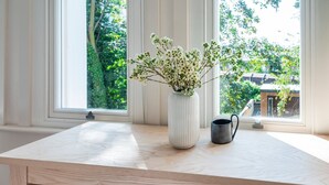 Una mesa de madera con un jarrón blanco y una taza negra sobre un alféizar.