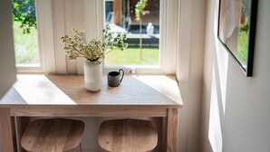 Una mesa de madera con dos taburetes, un jarrón blanco con flores y una taza negra.