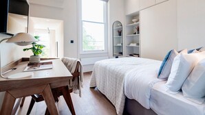 Un dormitorio moderno con un escritorio de madera, una cama con ropa blanca, un ventanal grande y estanterías empotradas.