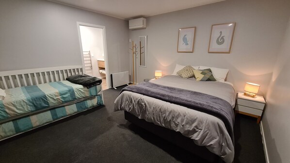 A bedroom with two beds, a radiator, a bedside table with a lamp, and two framed pictures on the wall. - Central Rotorua house with garden flat. Huge back yard, trampoline and fireplace (Rotorua)
