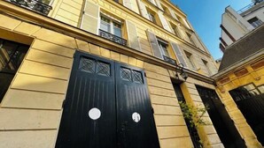 En byggnad med en svart dubbeldörr, en balkong och en krukväxt.