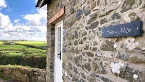 A stone building with a sign reading 'Sønn-y-Mør' and a white door. - Swn y Môr - 1 Bedroom Cottage - Whitesands (Saint David's and the Cathedral Close)