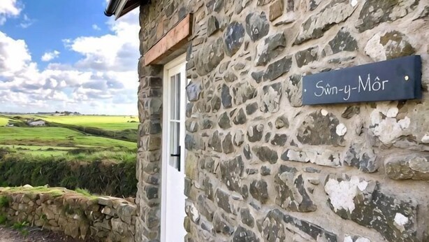 A stone building with a sign reading 'Sønn-y-Mør' and a white door. - Swn y Môr - 1 Bedroom Cottage - Whitesands (Saint David's and the Cathedral Close)