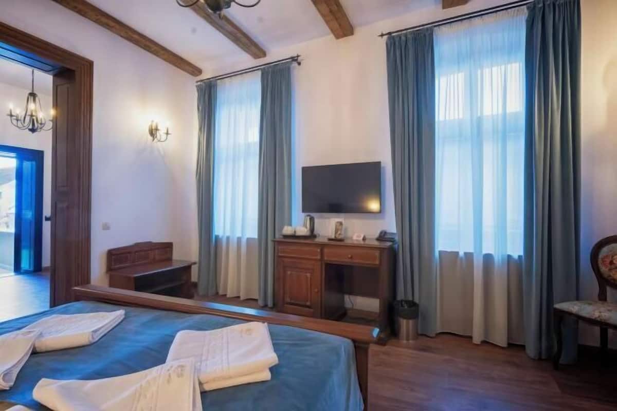 Habitación de hotel con cama, escritorio, televisor y ventanas grandes con cortinas.