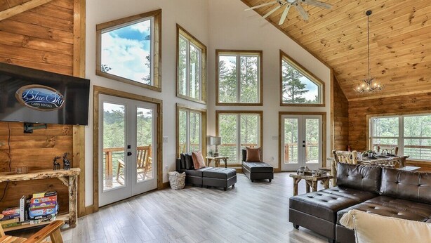 A spacious cabin interior with large windows, a fireplace, and a television. - Logan`s Lodge | Ellijay, GA (Ellijay)