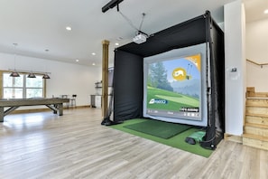 Huoneessa on biljardipöytä, projektorikangas, jolla näkyy golfpeli, ja vihreä matto lattialla.