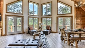 A spacious living room with a large sectional sofa, a dining table with chairs, and multiple large windows offering views of the outdoors. - Logan`s Lodge | Ellijay, GA (Ellijay)