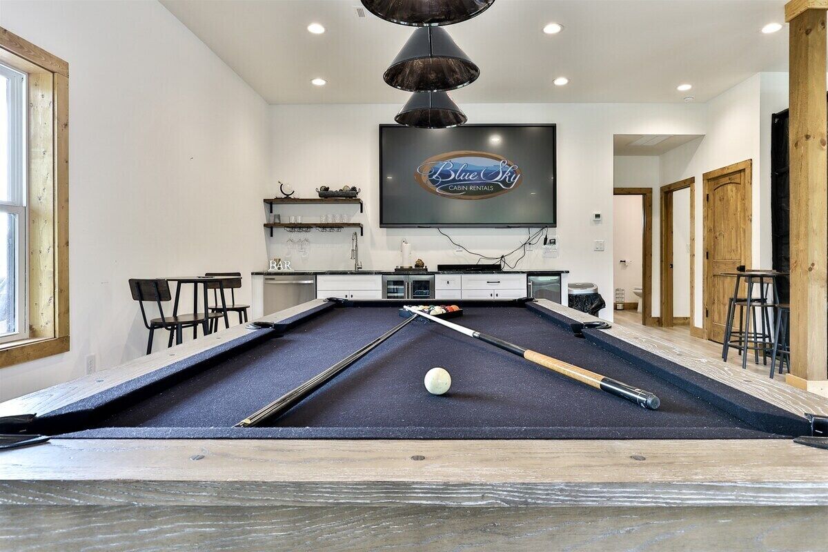 A pool table in a room with a television above it, a bar area, and wooden doors.