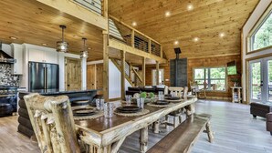 A spacious wooden interior with a long dining table, a kitchen area, and a staircase leading to an upper level. - Logan`s Lodge | Ellijay, GA (Ellijay)