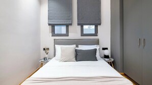 Ein modernes Schlafzimmer mit einem großen Bett, zwei Nachttischen, einem Kleiderschrank und zwei Fenstern mit Jalousien.