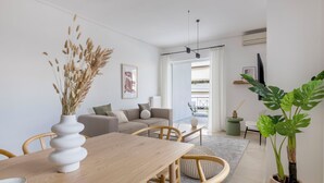 A modern living room with a wooden dining table, a sofa, and a large green plant. - Ample 3BR Apartment II in Marousi (Marousi)