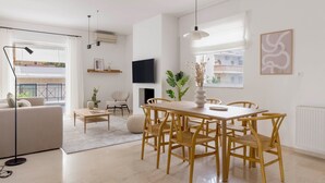 A modern living room with a dining area, featuring a sofa, a coffee table, a TV, and a fireplace. - Ample 3BR Apartment II in Marousi (Marousi)