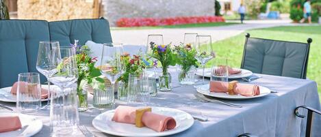 Een buiten eethoek met een tafel voor vier personen, voorzien van glazen, roze servetten en bloemstukken.