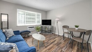A living room with a blue sofa, a round coffee table, a TV, a floor lamp, and a dining table with chairs. - Modern 1BR | First Floor | Garage | Rocky River (Rocky River)