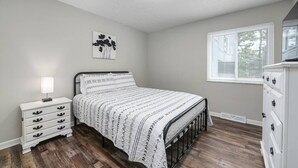 A bedroom with a bed, a nightstand, a dresser, a window with blinds, and a ceiling light. - Modern 1BR | First Floor | Garage | Rocky River (Rocky River)