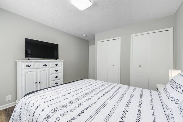 Une chambre à coucher avec un lit, un téléviseur posé sur une commode et deux placards.