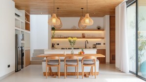 A modern kitchen with a central island, wooden chairs, and hanging pendant lights. - Loona Palm Villas by Villa Finder (Canggu)