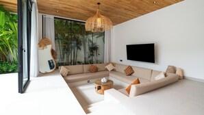 A modern living room with a large sectional sofa, a glass coffee table, and a hanging light fixture. - Loona Palm Villas by Villa Finder (Canggu)