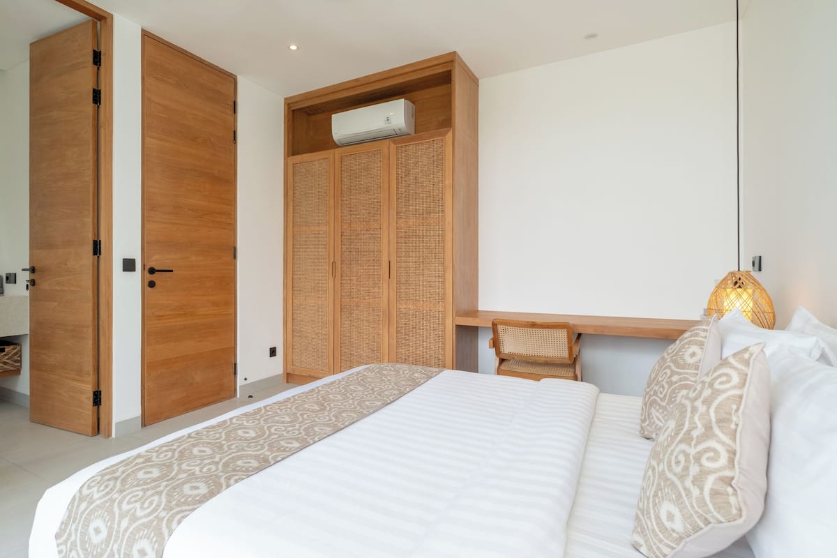 A bedroom with a bed, a wooden wardrobe, a ceiling fan, and a bedside table.
