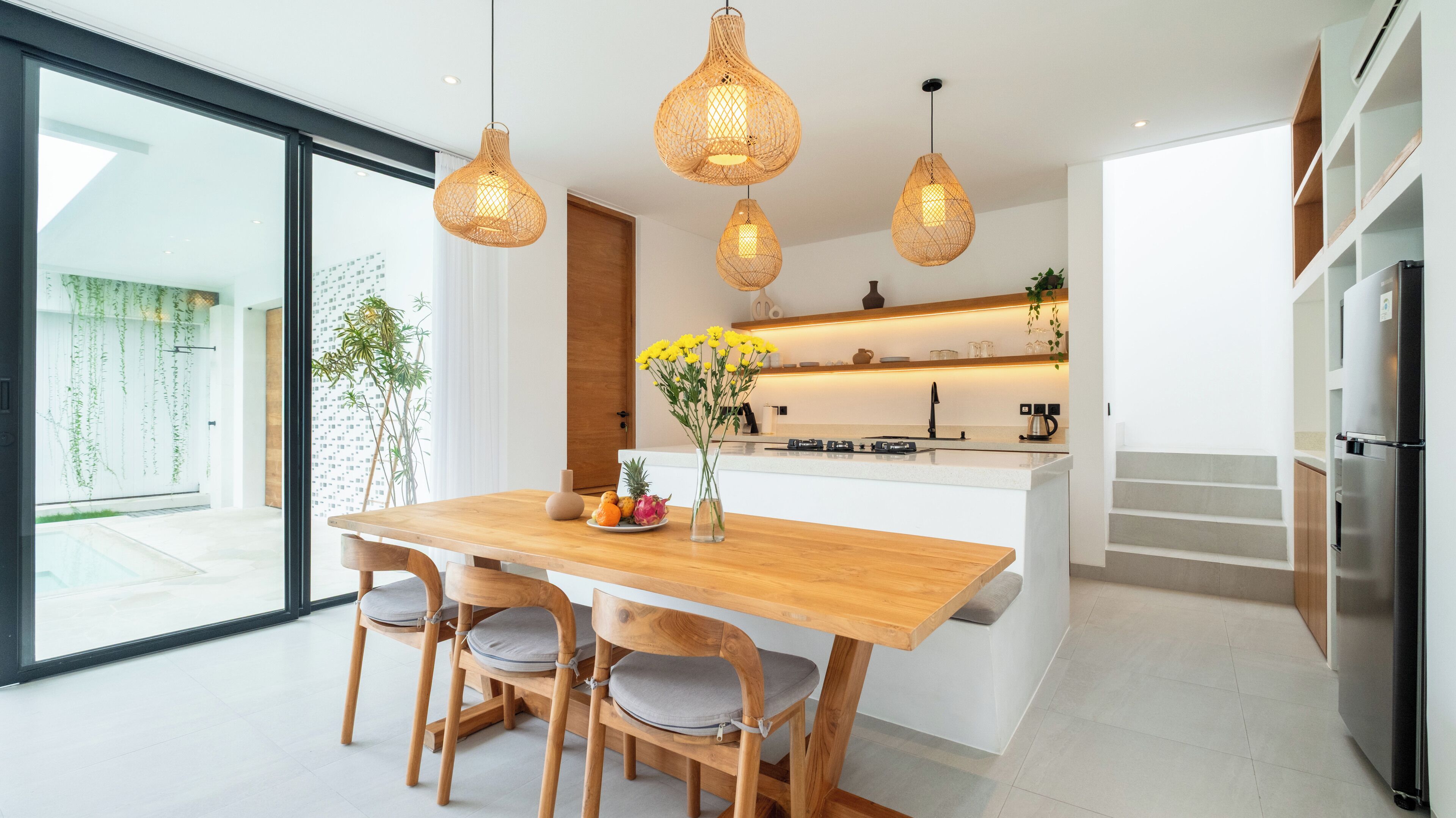 A modern kitchen with a wooden island, pendant lights, and a view to the outside.