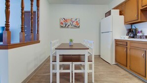 Une petite cuisine avec une table et des chaises en bois, un réfrigérateur et un coin café.