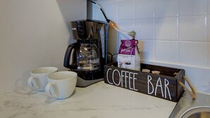 Un coin café aménagé avec une machine à café, deux tasses blanches et un paquet de café posés sur un comptoir.