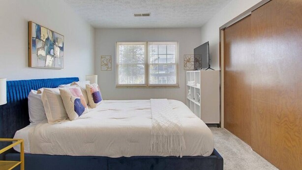Une chambre à coucher avec un lit, une armoire, une télévision et une fenêtre.