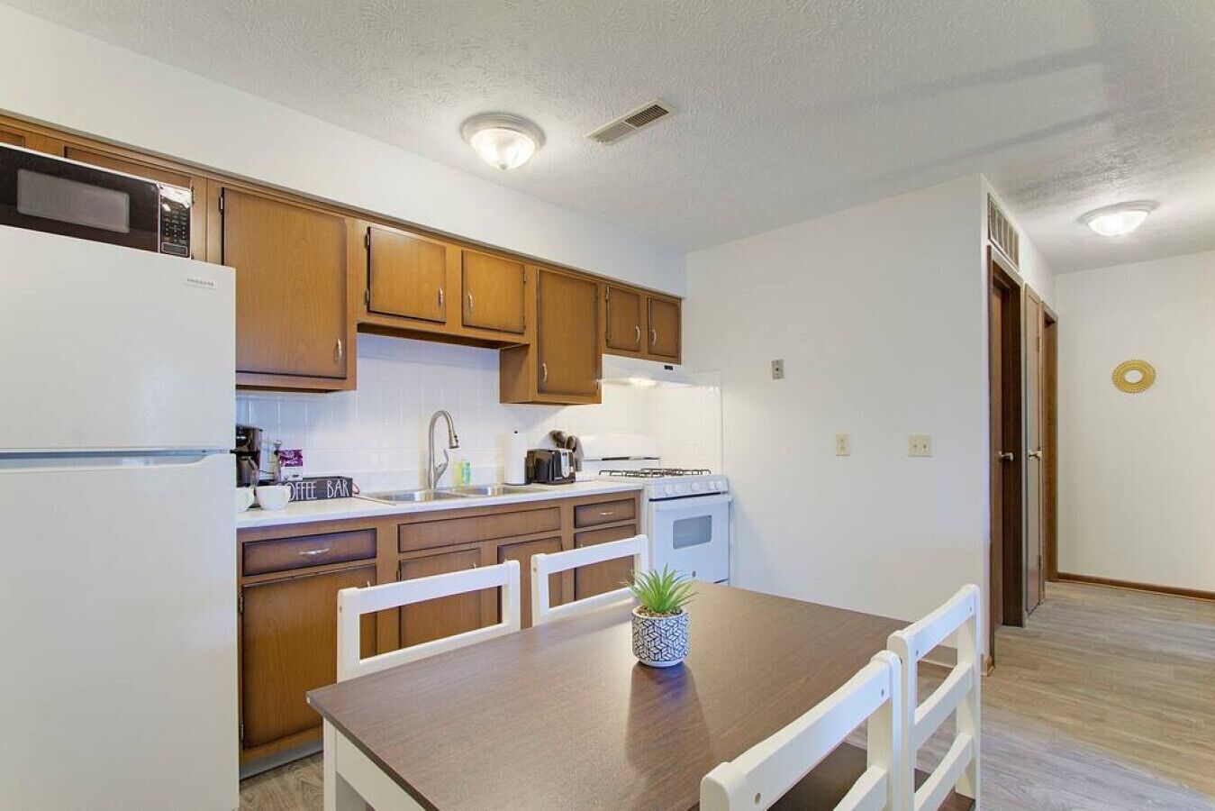 A compact kitchen with wooden cabinets, a white refrigerator, a stove, and a dining table with chairs.