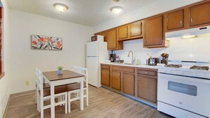 Une cuisine avec des meubles de rangement en bois, un réfrigérateur blanc, une cuisinière et une table à manger avec des chaises.