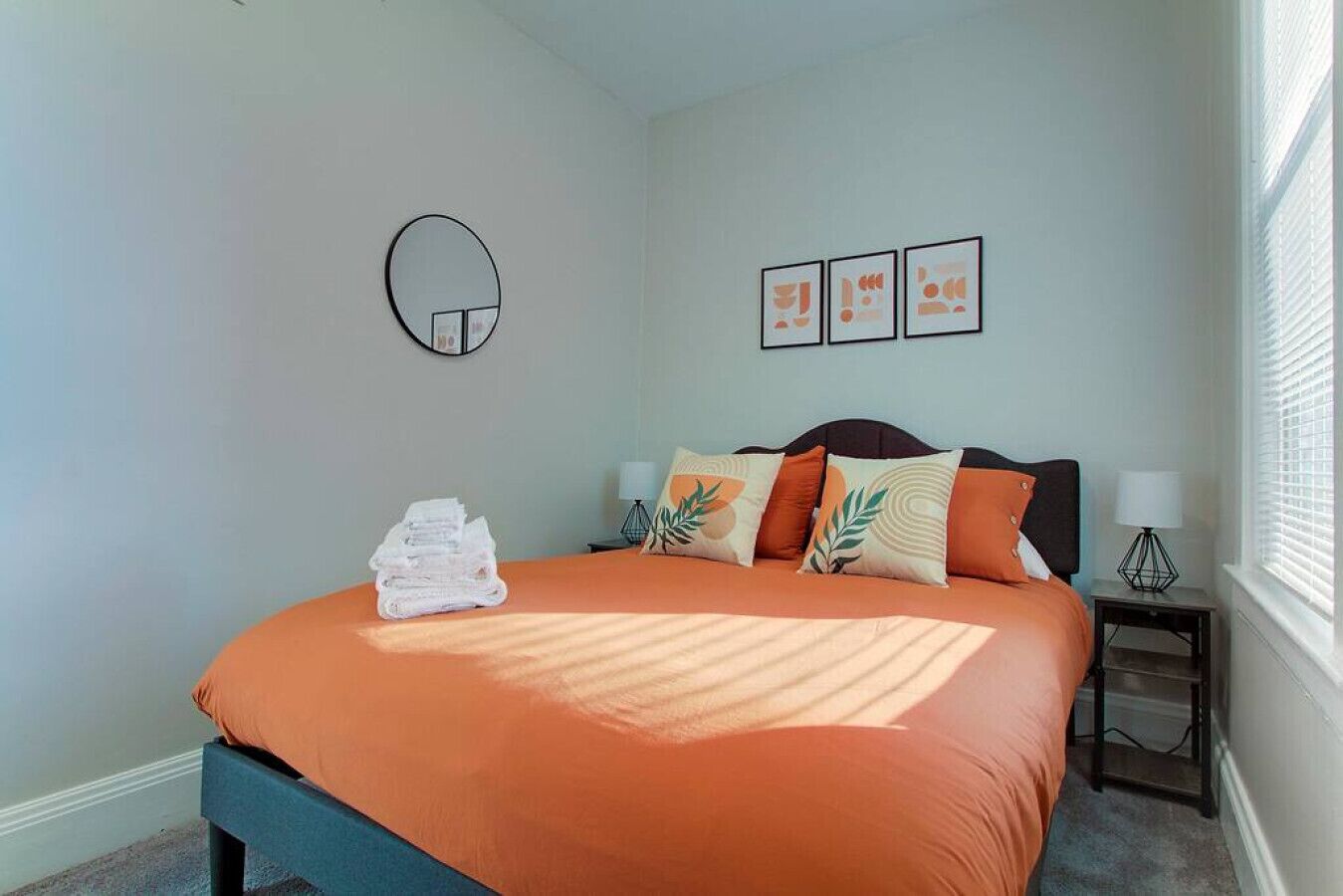 Una camera da letto con un letto, cuscini, un comodino, una lampada e una sveglia a muro.