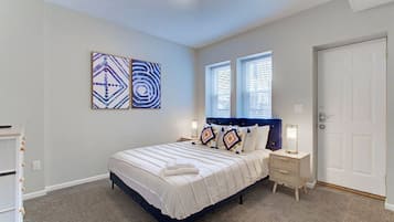 A bedroom with a bed, two bedside tables, a door, and two windows.