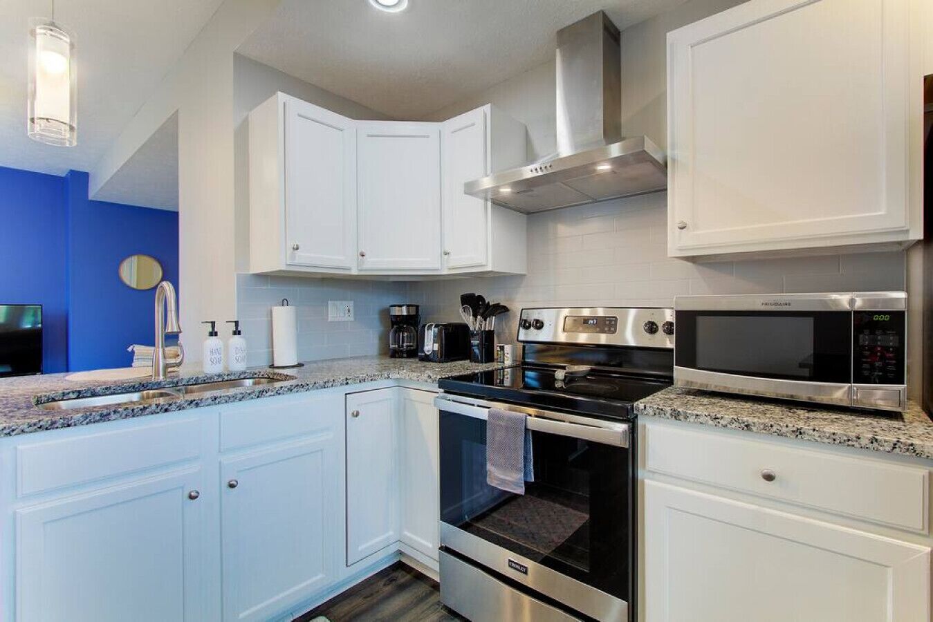 Une cuisine moderne avec des armoires blanches, des appareils en acier inoxydable et un mur d’accent bleu.