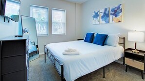 Een slaapkamer met een bed, nachtkastjes, een bureau, een stoel en kunst aan de muur.