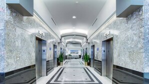 Un moderno vestíbulo de hotel con paredes de mármol, una zona central con baldosas y ascensores a ambos lados.