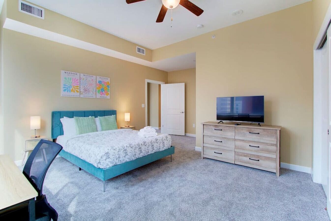 A bedroom with a bed, a dresser, a television, and a door.