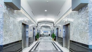 Un moderno vestíbulo de hotel con paredes de mármol, un piso central de baldosas y ascensores a ambos lados.