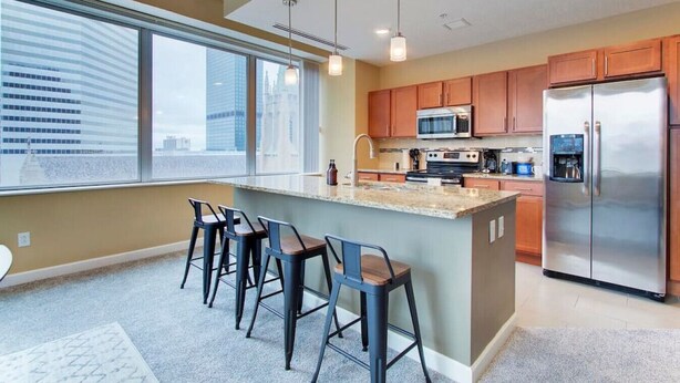 Una cocina moderna con una isla grande, taburetes de bar, electrodomésticos de acero inoxidable y vistas a la ciudad.