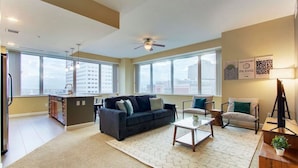 A spacious living room with a sofa, coffee table, and chairs, large windows with a city view, and a ceiling fan. - Luxury High Rise | Downtown | Free Parking (Cleveland)