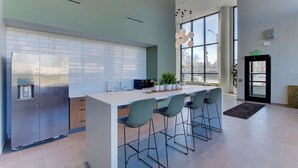 Cocina moderna con una isla central, taburetes de bar, un refrigerador de acero inoxidable y amplias ventanas que ofrecen luz natural.