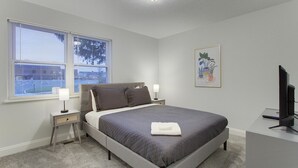 Ein Schlafzimmer mit einem Bett, Nachttischlampen, einem Fernseher und einem Fenster mit Jalousien.