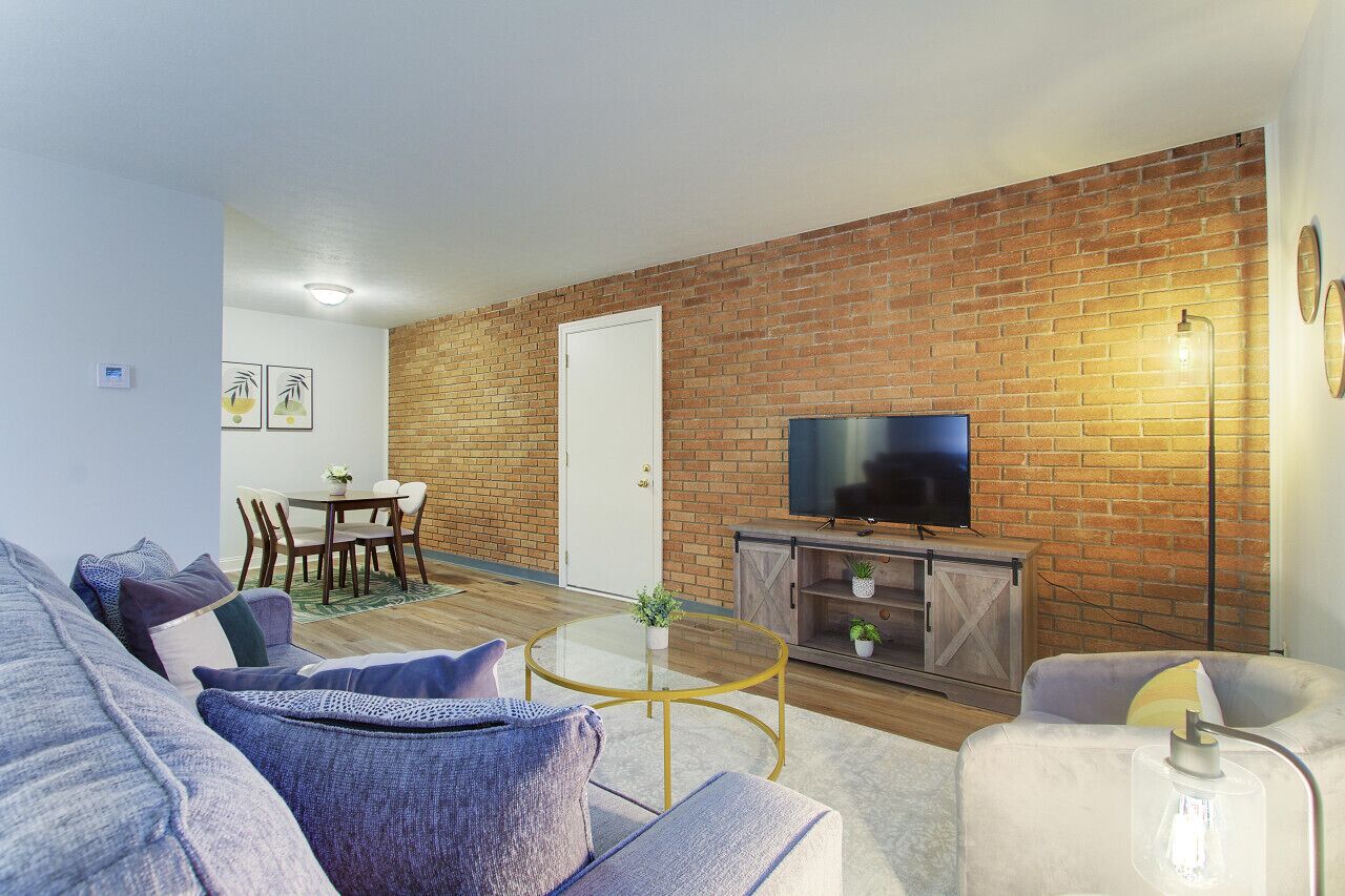 A living room with a brick wall, a flat-screen TV, a glass coffee table, and a sofa.