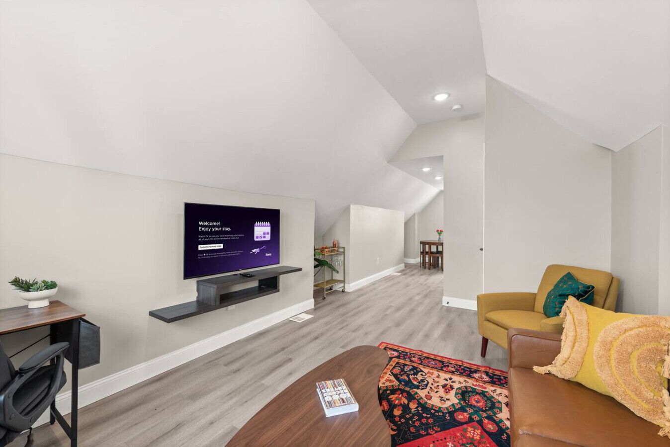 Una sala de estar moderna con un televisor de pantalla plana montado en la pared, un sofá, una mesa de centro y una mesita auxiliar con una planta.