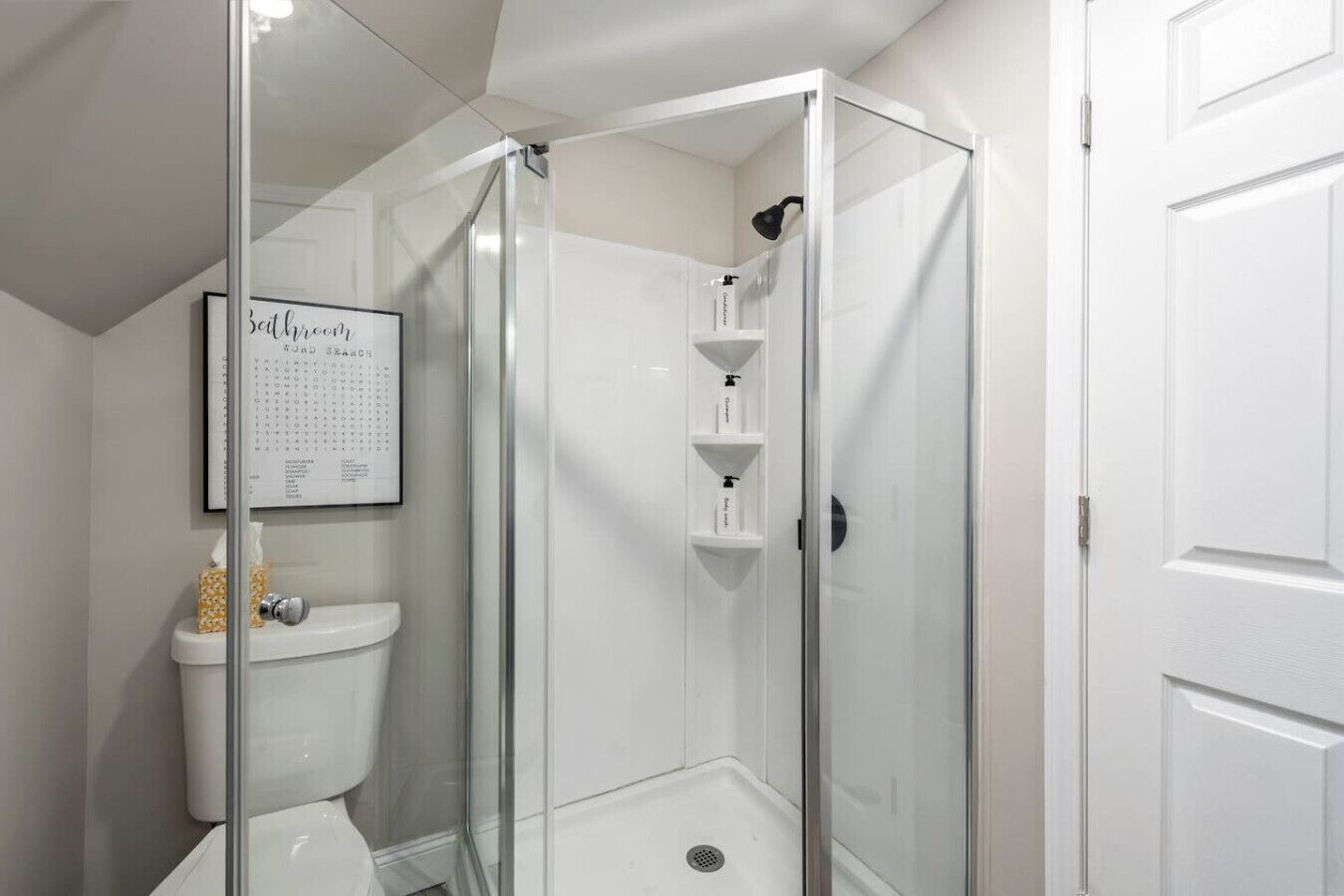 A modern bathroom with a glass-enclosed shower, a toilet, and a shelf with toiletries.