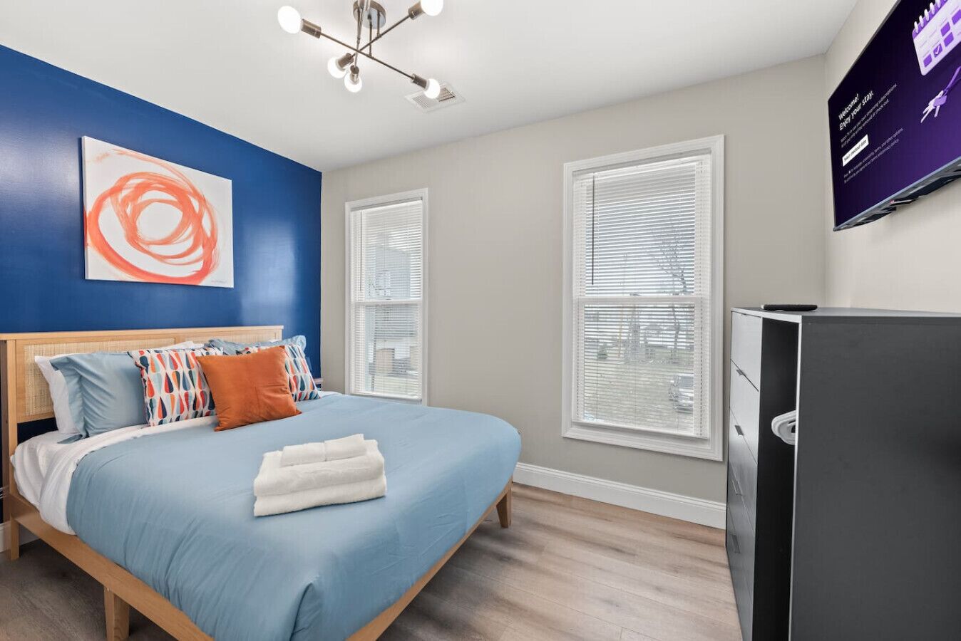 A bedroom with a bed, a TV, and a painting on the wall.