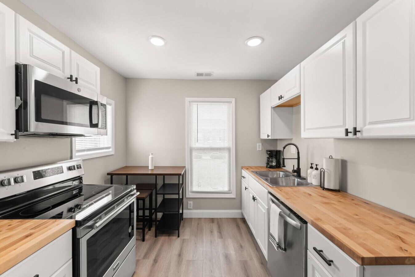A compact kitchen with white cabinets, a microwave, stove, and a sink.