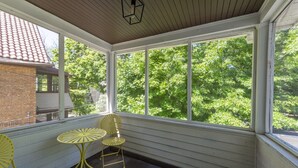 A covered porch with a table and chairs, large windows, and a view of trees. - 2BR Near Cleveland Clinic | Garage & Patio (Cleveland Heights)