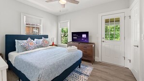 A bedroom with a bed, a ceiling fan, a TV, and a door. - 2BR Near Cleveland Clinic | Garage & Patio (Cleveland Heights)