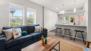 Uma sala de estar moderna com sofá, mesa de centro e banquetas de bar.