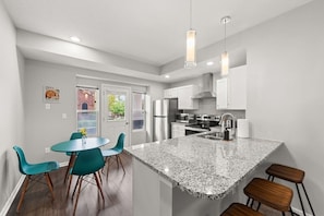 Une cuisine moderne avec un îlot en granit, des armoires blanches et des chaises de couleur turquoise.