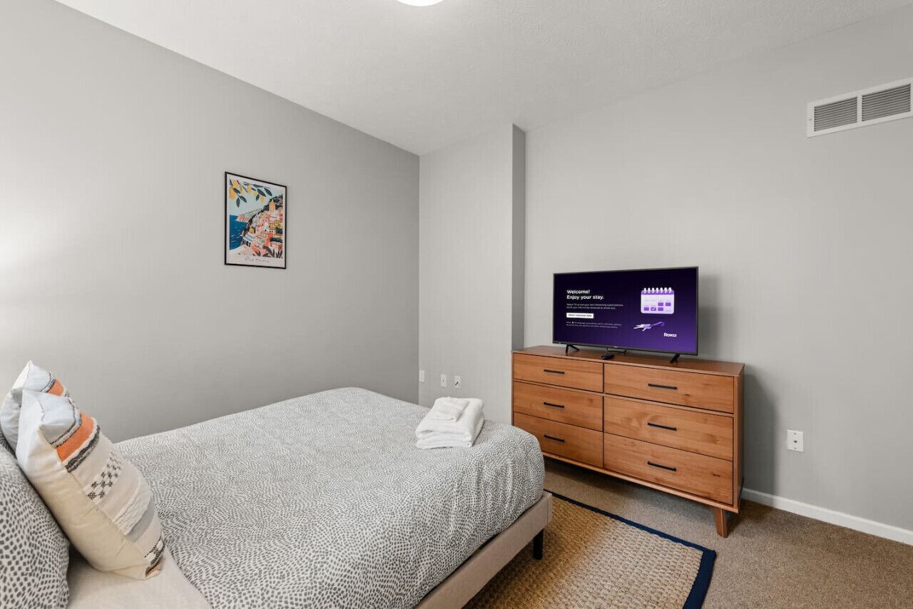Ein Schlafzimmer mit einem Bett, einer Holzkommode, einem Fernseher und einem Wandbild.
